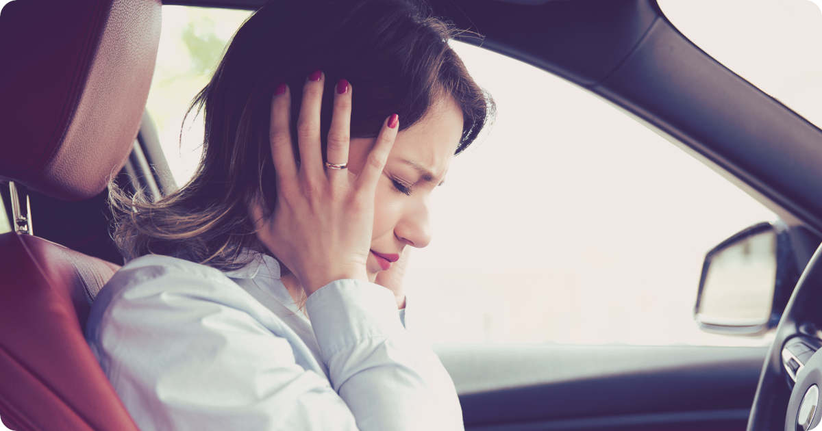 Eine Frau sitzt im Auto und hält sich die Ohren zu um den Windgeräuschen zu entgehen.