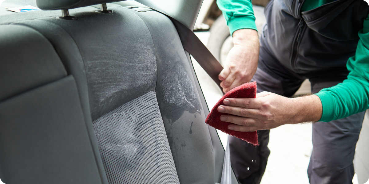 Ein Mann reinigt mit einem nassen Schwamm den hinteren Autositz.